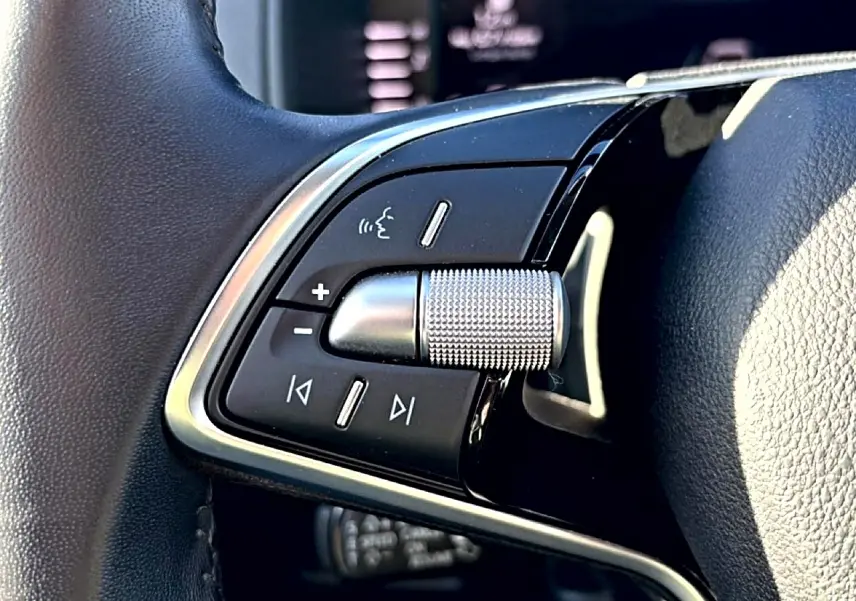 Gros plan sur les commandes audio au volant cuir noir d’un Skoda Karoq gris, version 2025, avec molette métallique texturée.