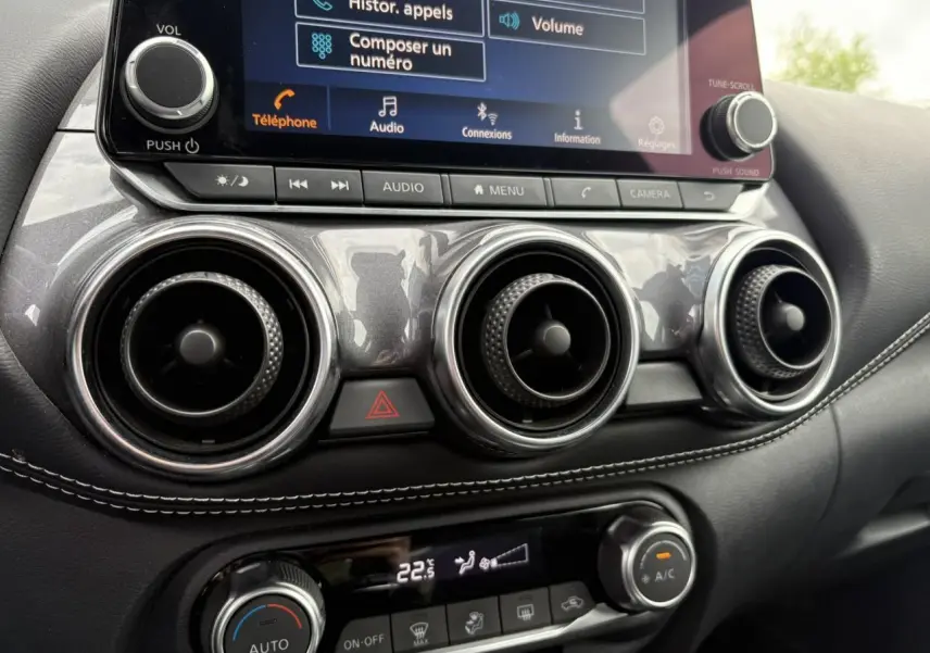Gros plan sur la console centrale du Nissan Juke blanc perle 2023, affichant l'écran tactile et les commandes de climatisation.