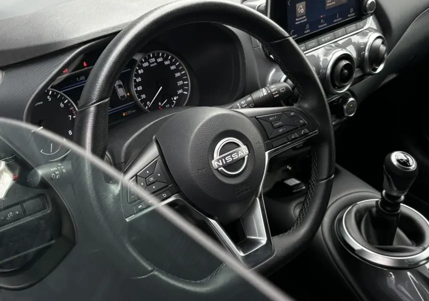 Vue rapprochée de l'intérieur du Nissan Juke blanc perle 2023, volant multifonction et levier de vitesse manuel visibles.