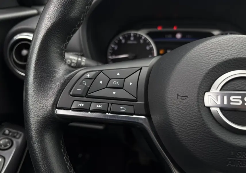 Gros plan sur le volant noir du Nissan Juke 2023 avec commandes intégrées côté gauche et logo central visible.