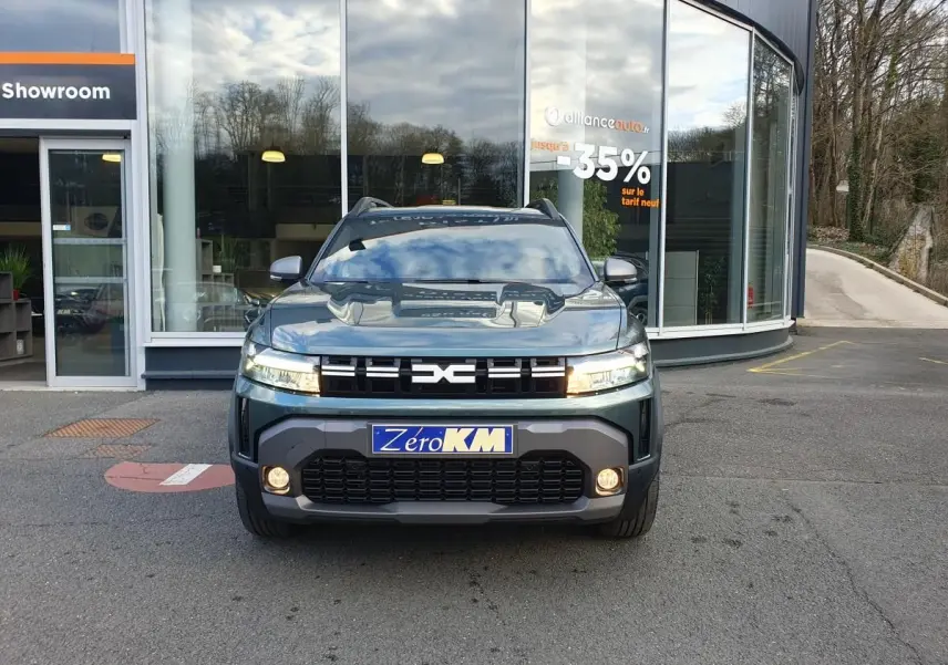 Vue frontale d'un Dacia Duster 2026 vert cèdre avec calandre noire et feux LED allumés devant un showroom.