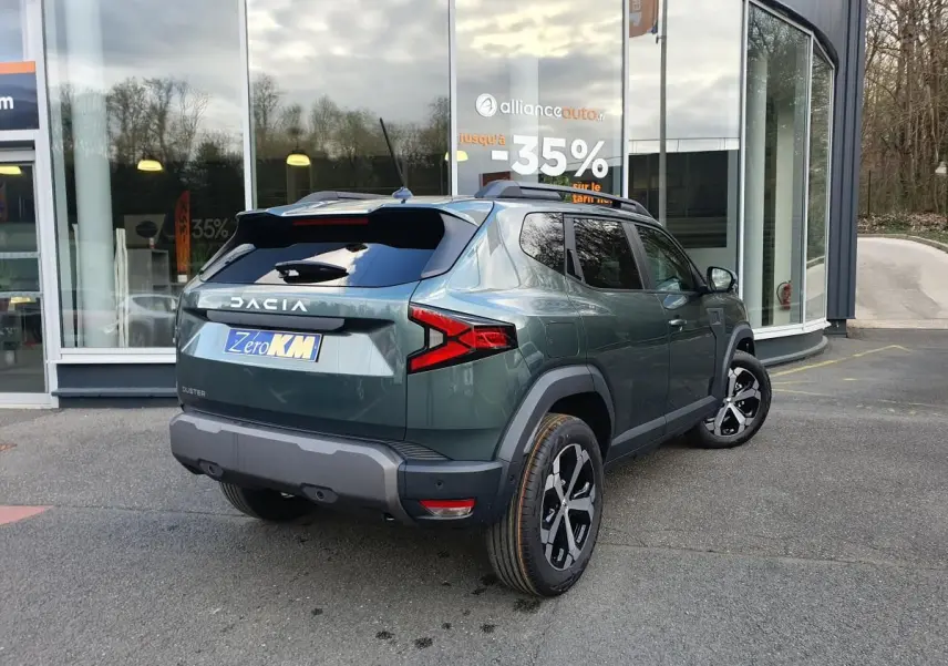 Vue 3/4 arrière droite du Dacia Duster vert cèdre 2026 avec jantes alliage 18” diamantées et barres de toit.