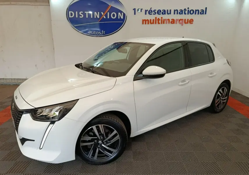 Peugeot 208 blanc vue 3/4 avant droit en intérieur, avec jantes alliage noires et feux LED distinctifs.