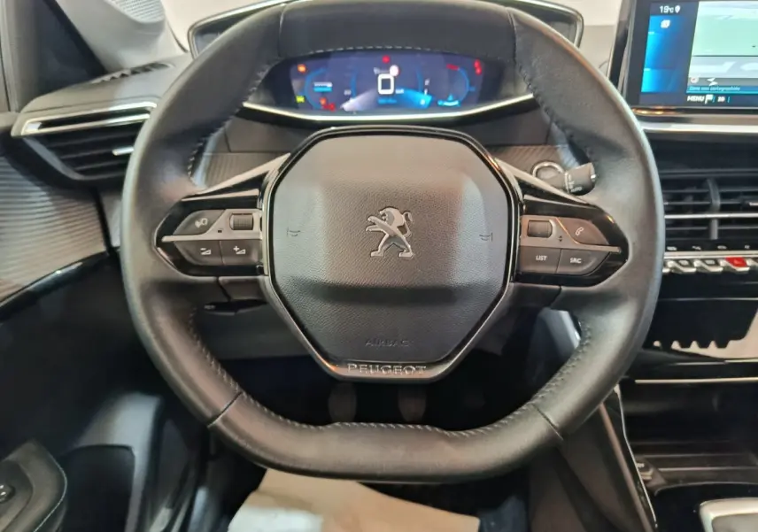 Vue rapprochée du volant cuir noir de la Peugeot 208 avec tableau de bord numérique et écran tactile visible à droite.