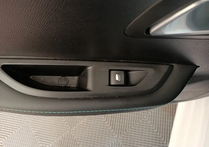 Détail de la commande de lève-vitre sur la porte intérieure noire avec surpiqûres bleues d’une Peugeot 208 blanche.