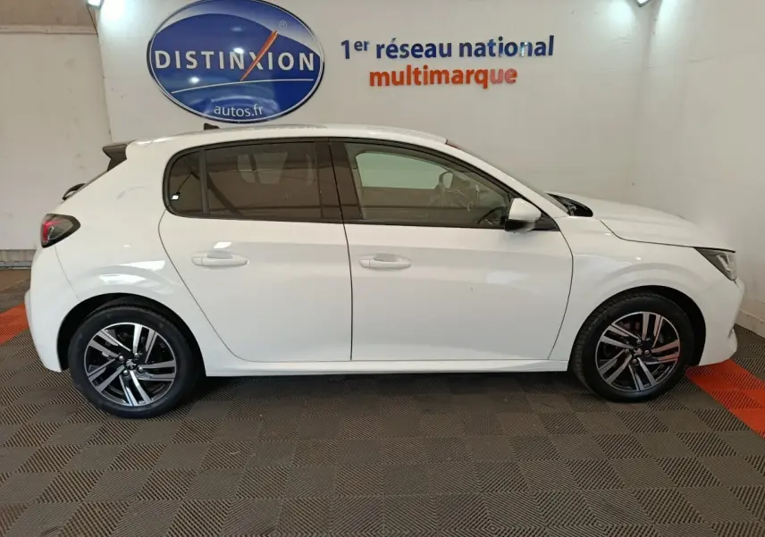 Vue latérale droite d'une Peugeot 208 blanche 2021 garée en intérieur, avec jantes alliage et vitres teintées.