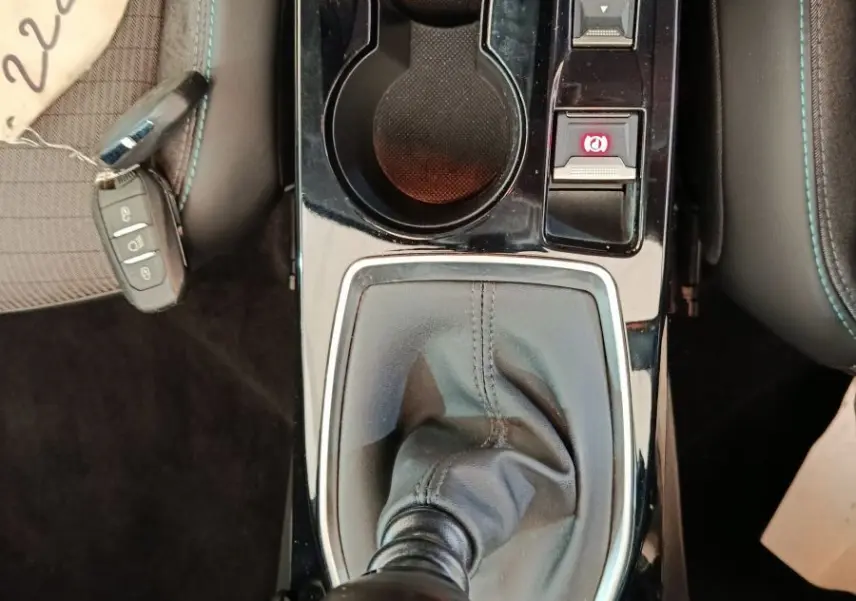 Vue plongeante sur la console centrale noire de la Peugeot 208 blanche, avec levier de vitesse manuel et porte-gobelets.