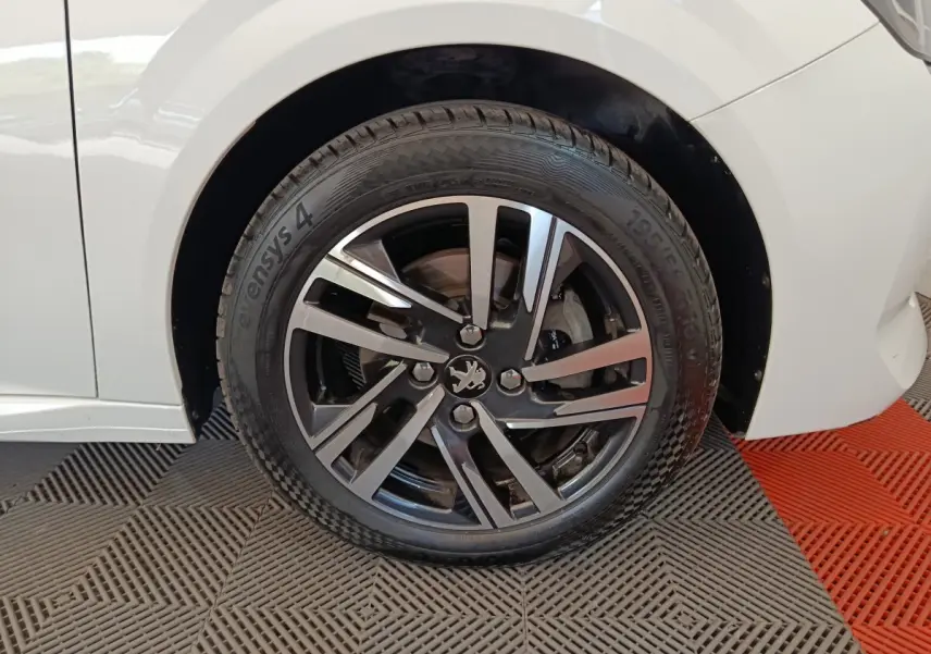 Gros plan sur la roue avant droite blanche d'une Peugeot 208 avec jante alliage noire et argentée.