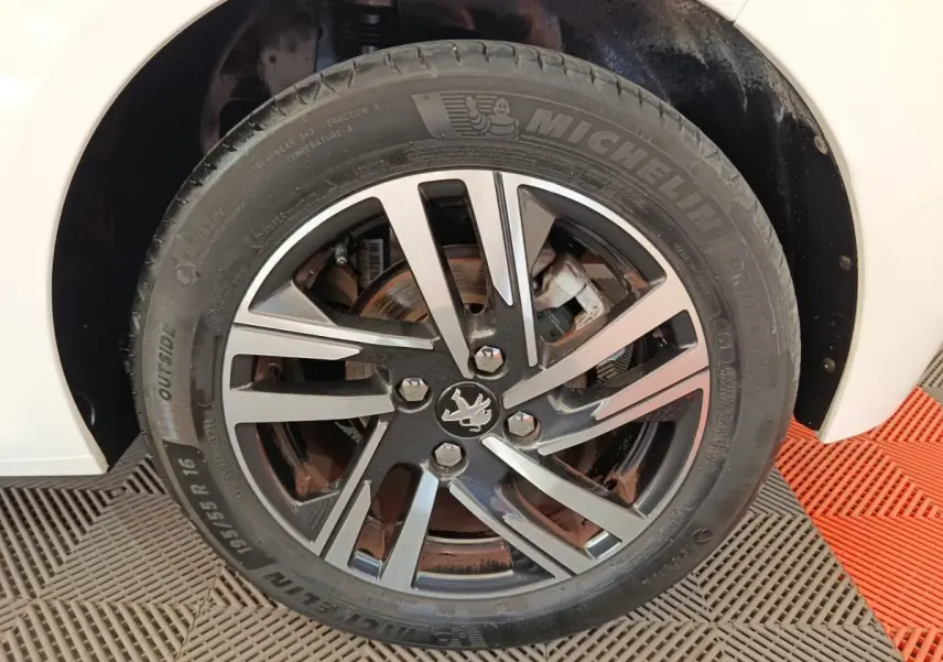 Gros plan sur la roue avant droite d'une Peugeot 208 blanche, mettant en valeur la jante alliage noire et argent.