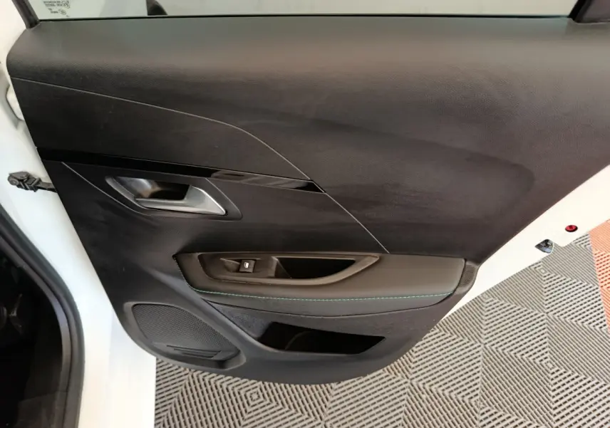Vue rapprochée de la porte avant gauche noire avec poignée argentée et bouton de lève-vitre sur Peugeot 208 blanc.