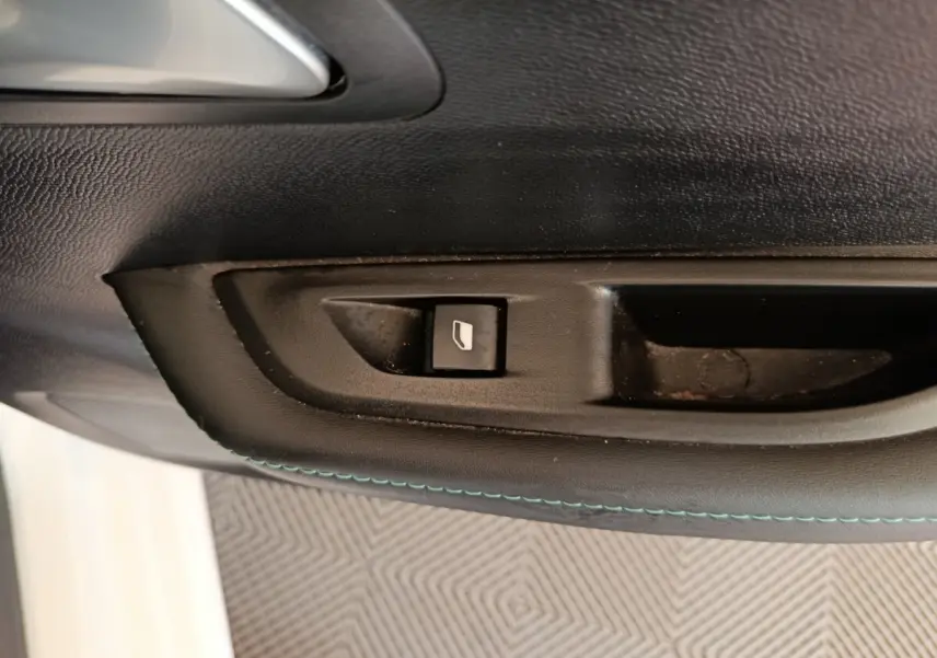 Gros plan sur le bouton de commande de la vitre côté conducteur, intérieur noir avec surpiqûres bleues, Peugeot 208 blanc.