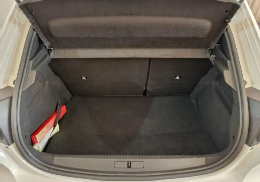 Coffre ouvert vu de face d’une Peugeot 208 blanche, intérieur noir avec un kit de sécurité rouge à gauche.