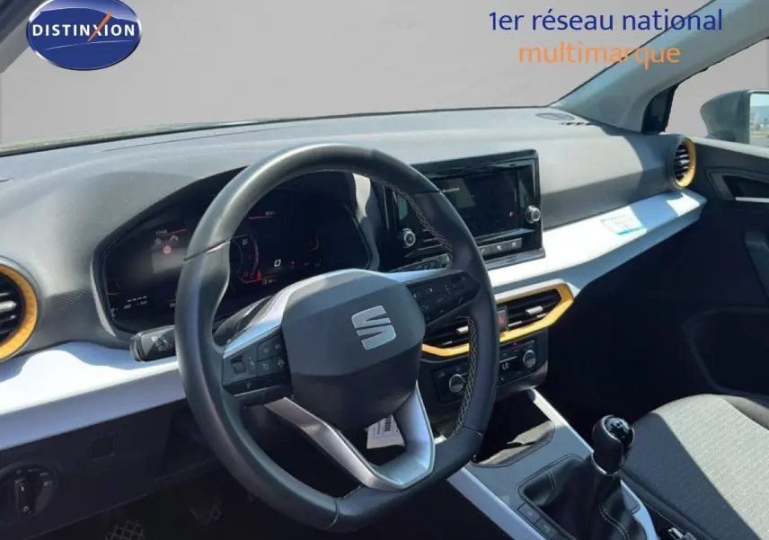Vue intérieure du poste de conduite du SEAT Arona 2025, volant cuir multifonction et tableau de bord avec inserts jaunes.