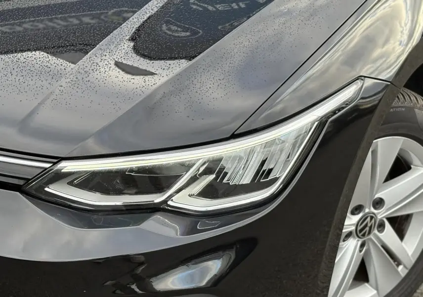 Vue intérieure côté conducteur de la Volkswagen Golf VIII noire, montrant sièges tissu et tableau de bord moderne.