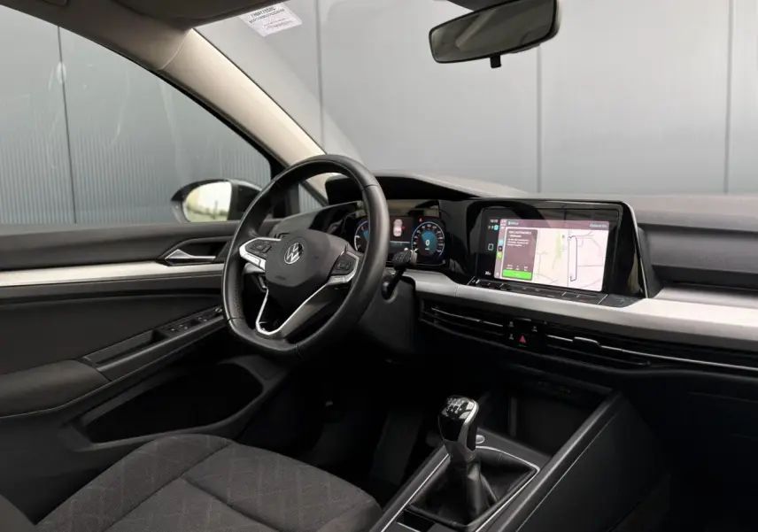 Coffre ouvert d'une Volkswagen Golf VIII noire vue de l'arrière, avec tapis de coffre et banquette arrière visible.