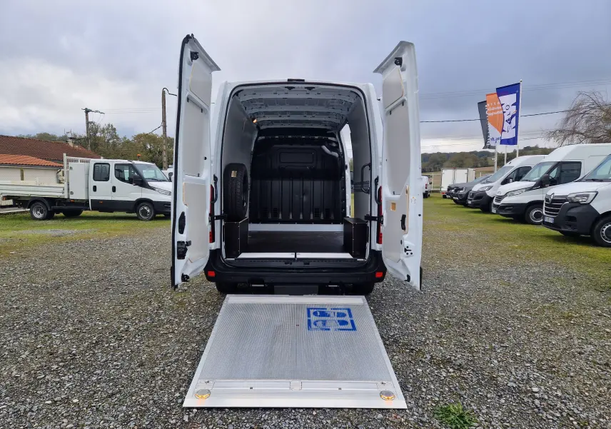 Vue arrière d’un Renault Master blanc 2023 avec hayon élévateur déployé et portes arrière ouvertes sur un parking.