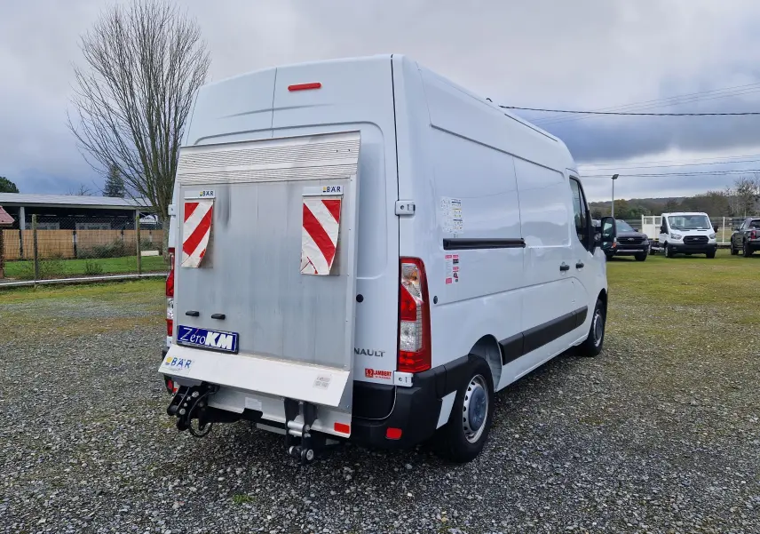 Vue 3/4 arrière droite d'un Renault Master blanc 2023 avec hayon élévateur et marquages de sécurité rouges.