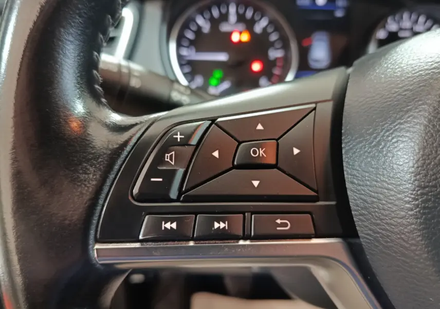 Gros plan sur les commandes multifonctions du volant en cuir noir du Nissan Qashqai 2019, avec tableau de bord flou en arrière-plan.