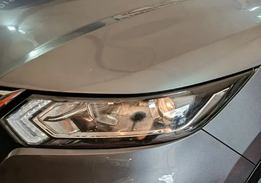 Gros plan sur le phare avant droit du Nissan Qashqai gris clair, mettant en valeur le design moderne et les détails lumineux.