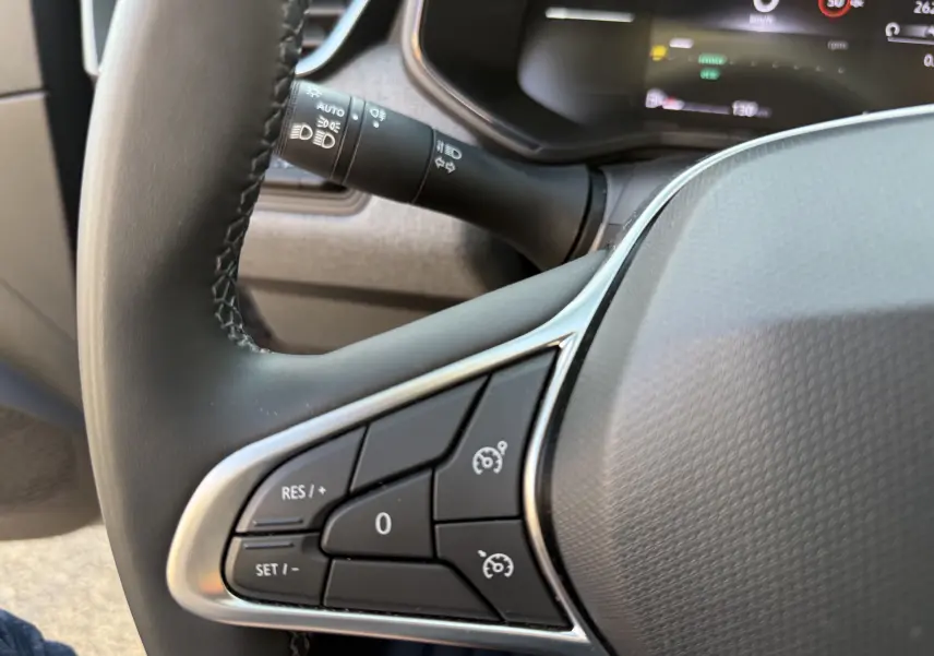 Gros plan sur les commandes au volant côté gauche d’une Renault Clio V gris schiste, avec tableau de bord numérique en arrière-plan.