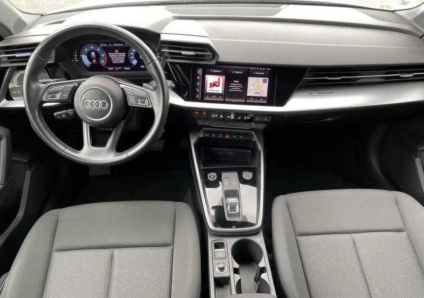 Vue intérieure de l'Audi A3 Sportback 2021 montrant le tableau de bord moderne avec écran tactile et volant cuir multifonctions.