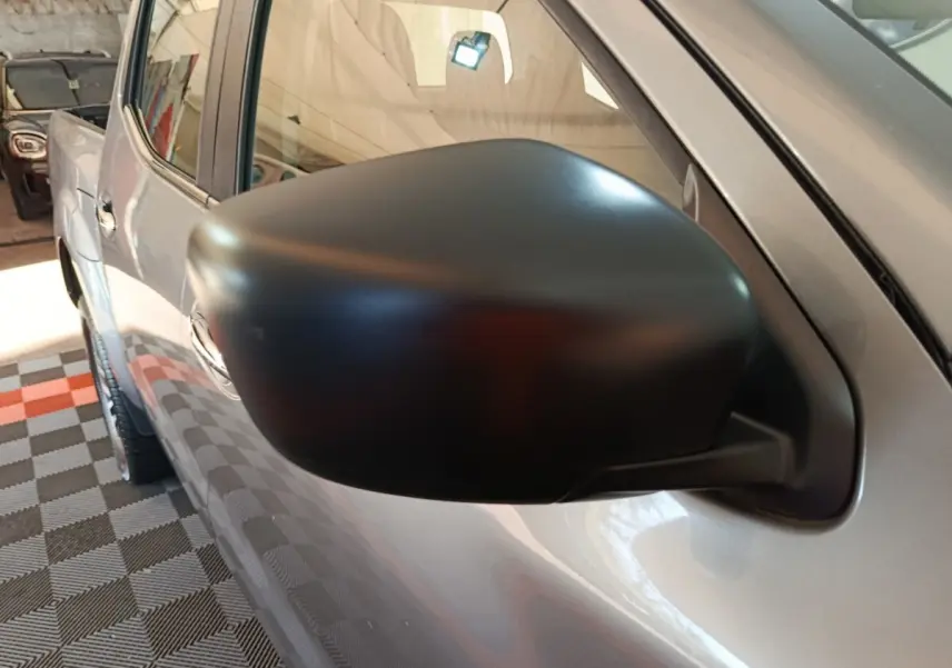Gros plan sur le rétroviseur côté gauche noir mat du Nissan Navara gris clair, vue partielle de la porte avant.
