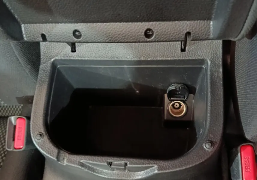 Vue rapprochée de la console centrale noire du Nissan Navara avec prise allume-cigare et bouton de frein à main visible.