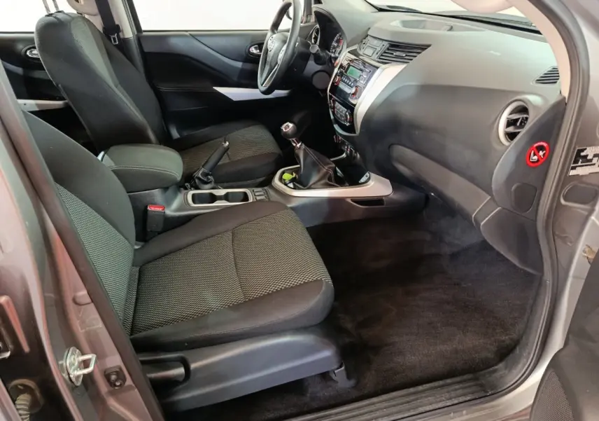 Vue intérieure côté passager avant du Nissan Navara gris clair 2018, montrant sièges noirs et tableau de bord avec boîte manuelle.