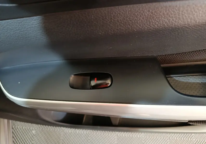 Gros plan sur le bouton de verrouillage de porte noir dans l'habitacle du Nissan Navara gris clair, côté intérieur.