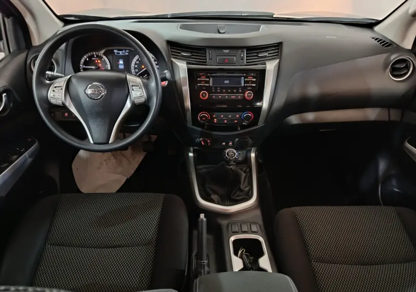 Vue intérieure frontale du tableau de bord du Nissan Navara gris clair, volant multifonctions et levier de vitesse manuel visibles.