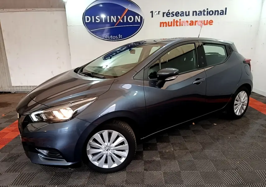 Nissan Micra IG-T 100 Business Edition gris foncé vue de profil droit en intérieur avec phares allumés.