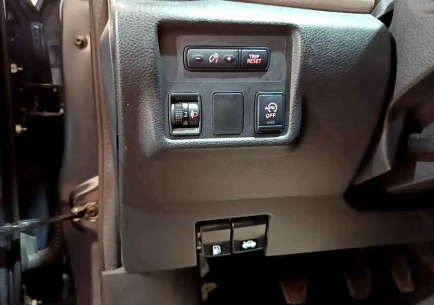 Vue rapprochée du tableau de bord côté gauche d’une Nissan Micra gris foncé, avec commandes d’éclairage et ouverture capot/essence.