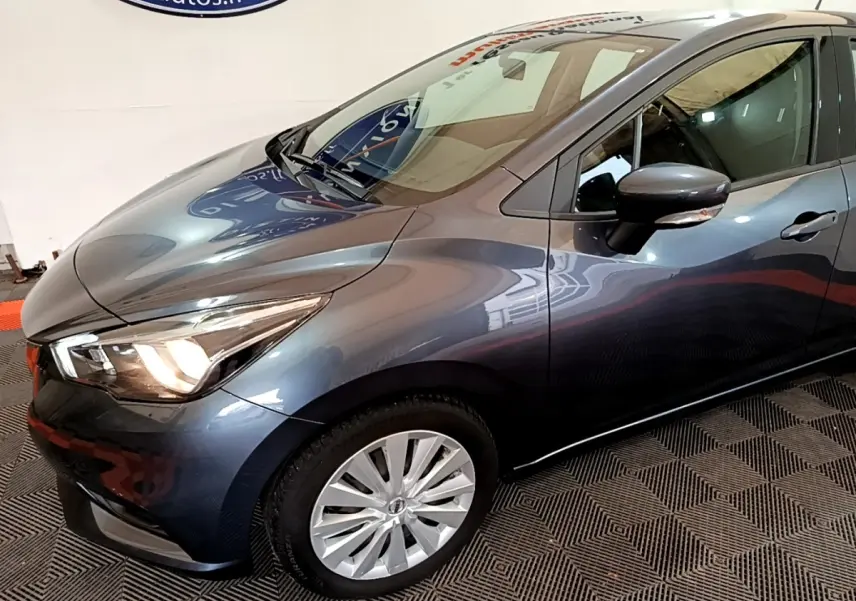 Vue 3/4 avant droit d'une Nissan Micra IG-T 100 Business Edition gris foncé avec phares allumés et jantes argentées.