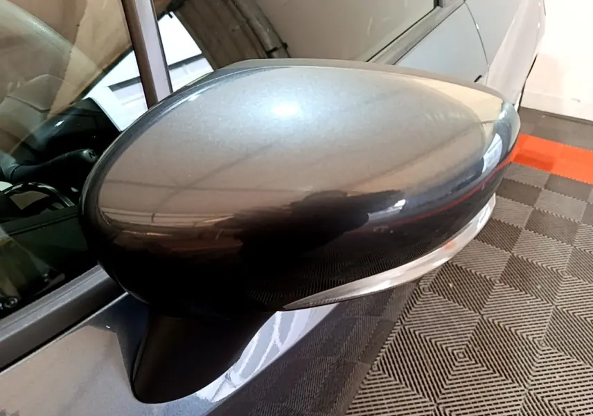 Gros plan sur le rétroviseur droit gris foncé de la Nissan Micra IG-T 100 Business Edition, avec reflet et partie de la portière visible.