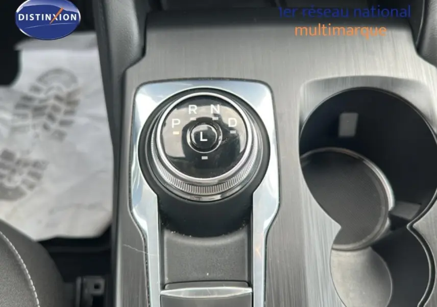 Gros plan sur la molette de boîte automatique du Ford Kuga blanc, avec porte-gobelets et console en finition métal brossé.