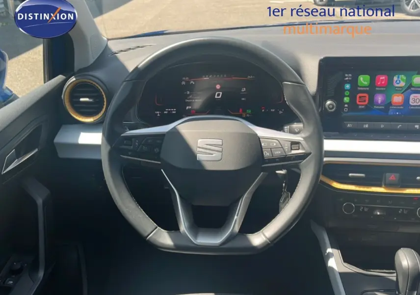 Vue intérieure centrée sur le volant du SEAT Arona 2025, tableau de bord numérique et écran tactile visibles.