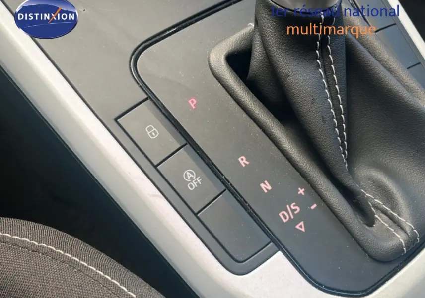 Gros plan sur la console centrale avec levier de vitesse automatique et coutures blanches sur tissu noir.