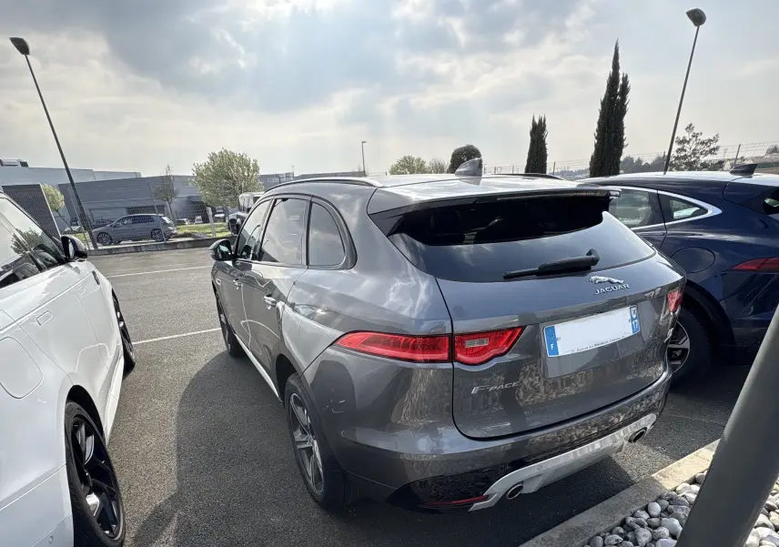 Jaguar F-PACE 3.0D 300 S gris ammonite vue 3/4 arrière droit sur parking avec feux arrière LED allumés.