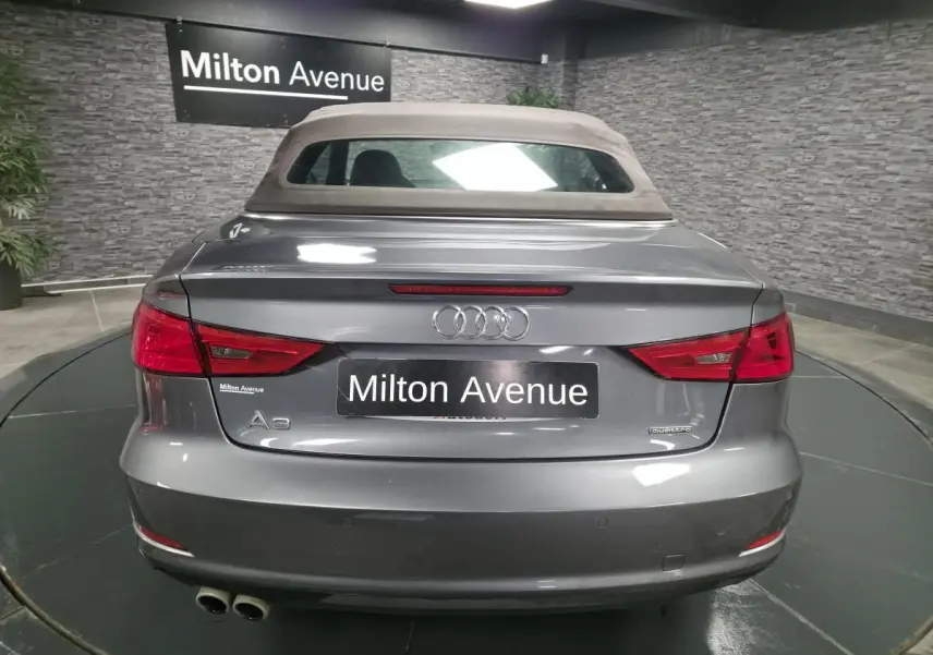 Vue arrière d'une Audi A3 Cabriolet gris foncé avec capote tissu beige et double sortie d'échappement chromée.