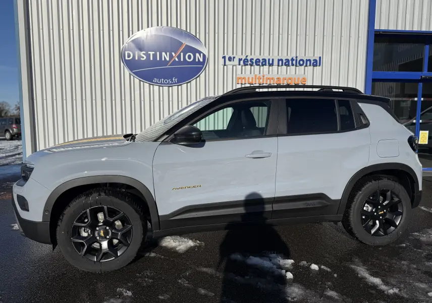 Vue de profil côté gauche d'un Jeep Avenger Storm Grey avec toit noir et jantes noires, stationné devant un bâtiment.
