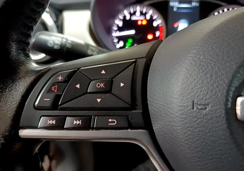 Gros plan sur le volant cuir noir de la Nissan Micra 2017, avec commandes multifonctions et tableau de bord flou en arrière-plan.