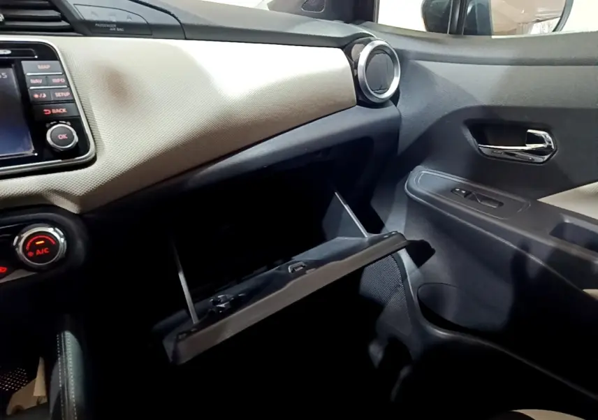 Vue intérieure côté passager de la Nissan Micra noire, boîte à gants ouverte et tableau de bord clair texturé.