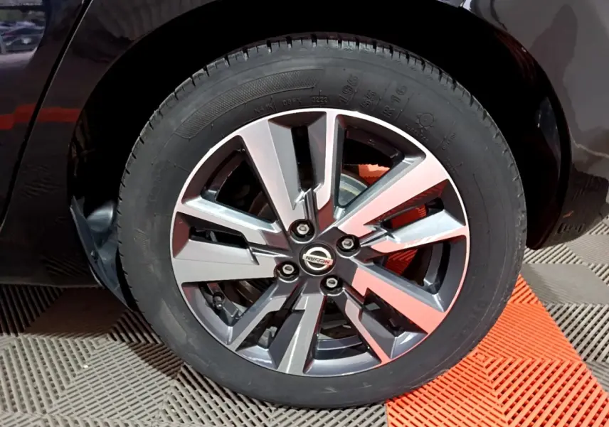 Gros plan sur la roue avant droite de la Nissan Micra noire, mettant en valeur la jante alliage au design moderne.