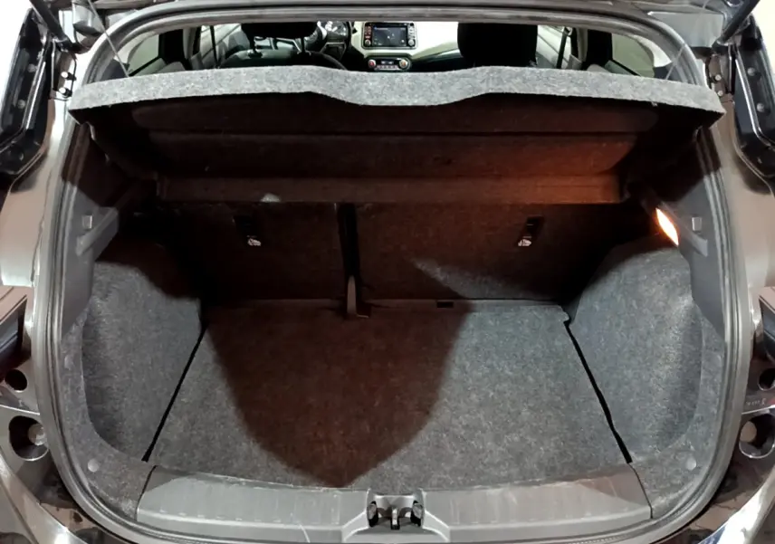 Coffre ouvert vu de l'arrière d'une Nissan Micra noire, intérieur du coffre en tissu gris avec tablette relevée.