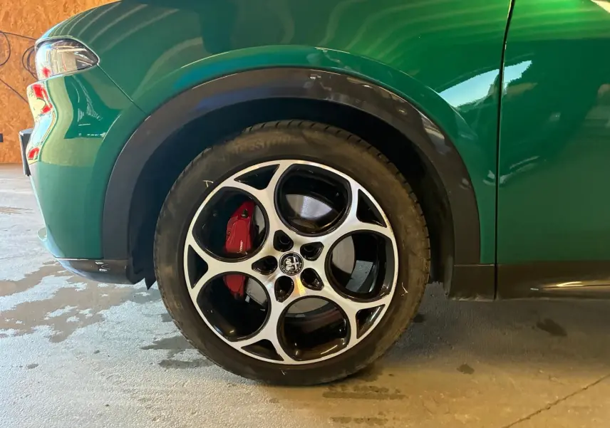 Gros plan sur la roue avant gauche d'une Alfa Romeo Tonale vert foncé avec étrier de frein rouge et jante noire et argent.
