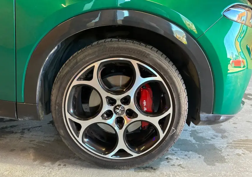 Gros plan sur la roue avant droite d’un Alfa Romeo Tonale vert foncé avec étrier de frein rouge et jante à cinq cercles.