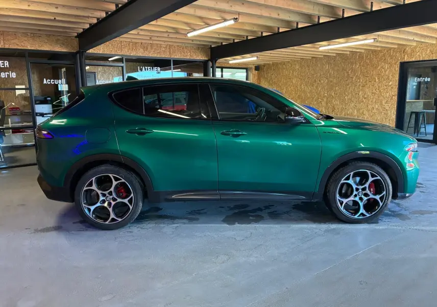 Vue de profil côté gauche d'une Alfa Romeo Tonale vert foncé avec jantes sport et freins rouges, stationnée en intérieur.