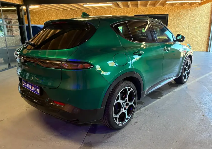 Vue 3/4 arrière droite d'une Alfa Romeo Tonale vert foncé avec jantes distinctives à cinq cercles, stationnée en intérieur.