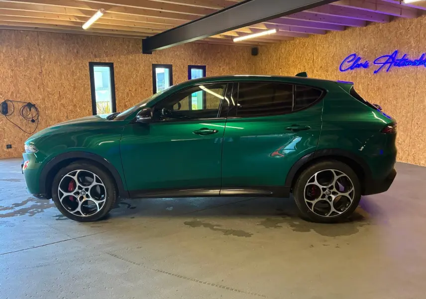 Vue de profil côté gauche d'un Alfa Romeo Tonale vert foncé avec jantes distinctives en intérieur bois.
