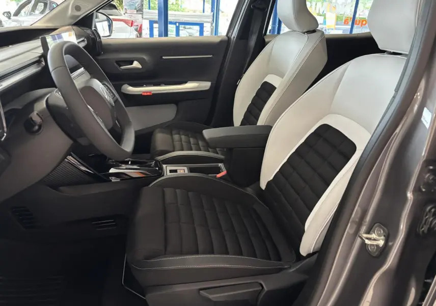 Vue intérieure côté conducteur du Citroën C3 Aircross 2026 gris, sièges bicolores noir et blanc avec accoudoir central.